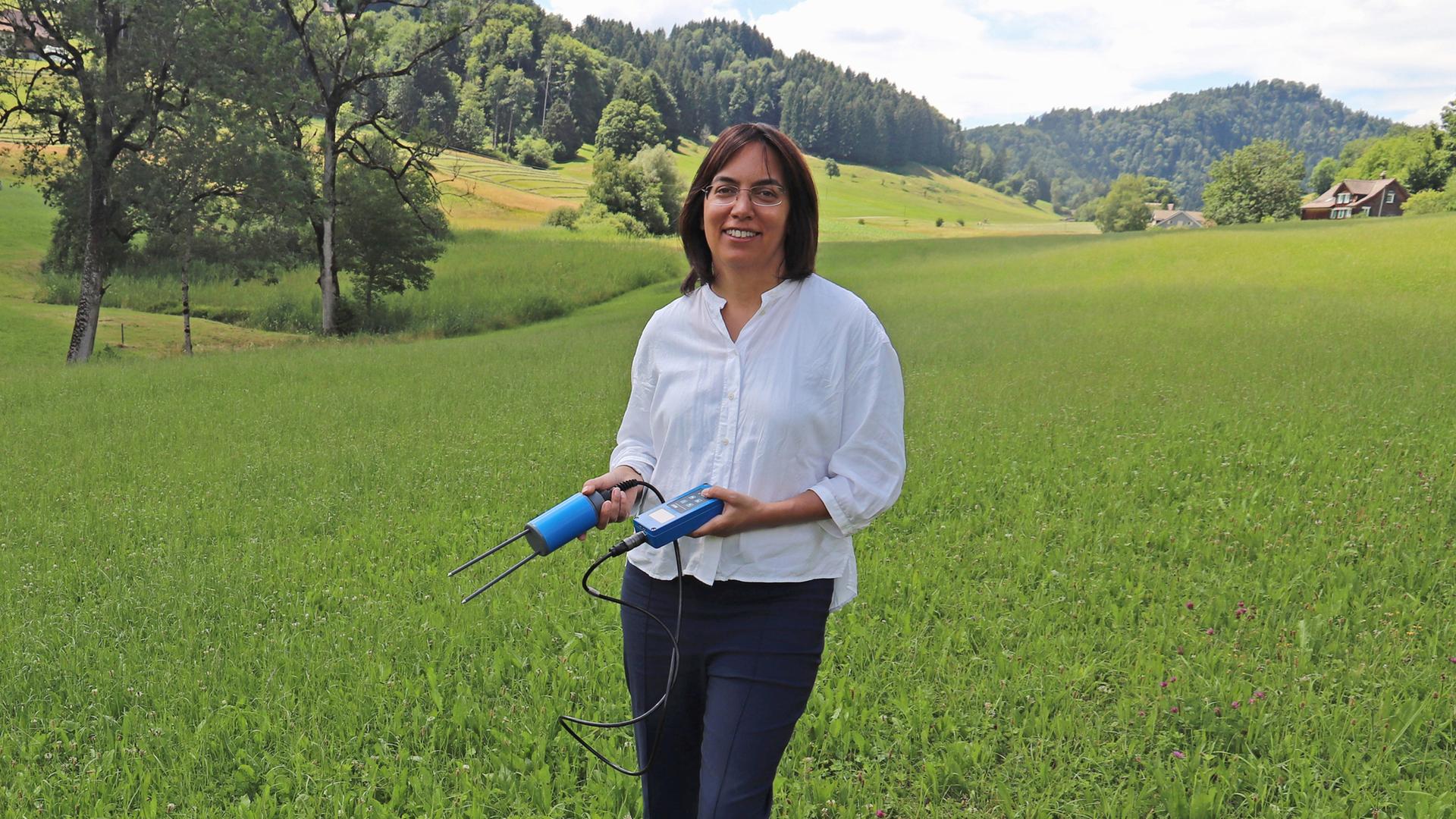 Die Schweizer Klimaforscherin Sonia Isabelle Seneviratne steht mit einem Bodenfeuchtemessgerät auf einer Wiese im Schweizer Voralpenland