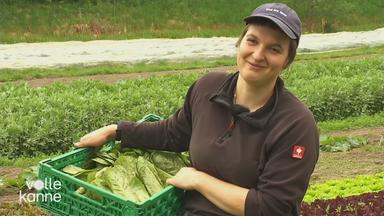Eine Frau auf dem Feld mit einer Gemüsekiste in der Hand.