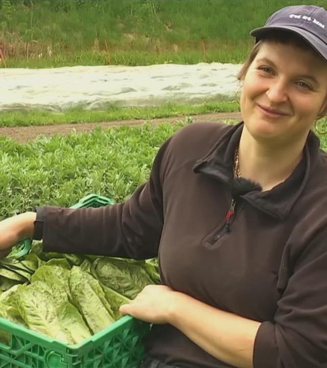 Eine Frau auf dem Feld mit einer Gemüsekiste in der Hand.