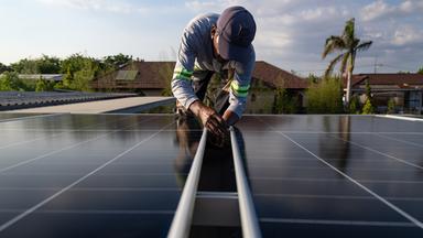 Zu sehen ist ein Mann der in einer knienden Position ein Solarmodul inspiziert.