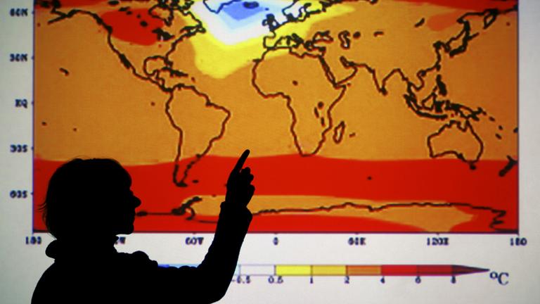 Eine Frau zeigt auf eine projizierte Karte der Welt mit einer Erderwärmungs-Simulation für das Jahr 2470.