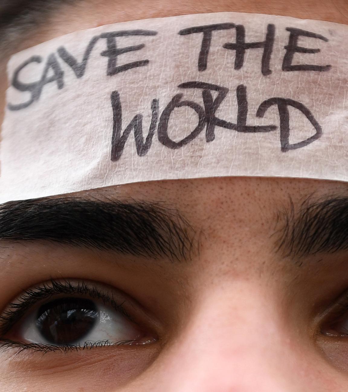 Ein Mädchen mit braunen Haaren hat ein weißes Klebeband auf der Stirn. Darauf steht: Save the world.