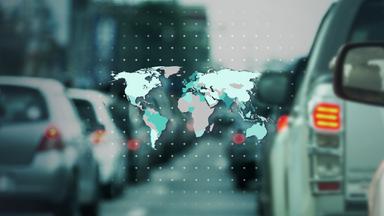 Umrisse einer Weltkarte mit unterschiedlich eingefärbten Ländern vor einem angedeuteten Punkteraster, im Hintergrund unscharf Schlangen von Autos auf einer Straße.