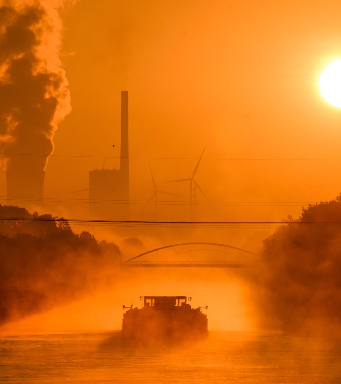 Symbolbild: Ein Schiff fährt auf dem Mittellandkanal durch den vom Sonnenaufgang in warmes Licht gefärbten Frühnebel in Richtung des Kraftwerks Mehrum im Landkreis Peine.  