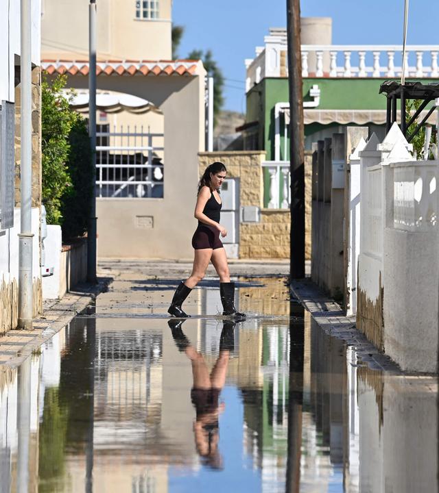 Eine Frau in Gummistiefeln überquert nach sintflutartigen Regenfällen eine Straße in Ostspanien.