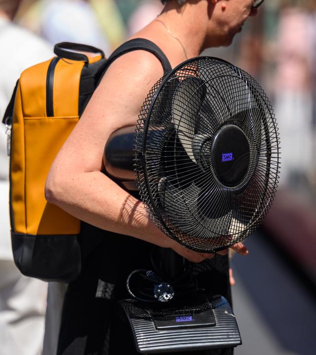Eine Frau trägt einen Ventilator unter ihrem Arm.
