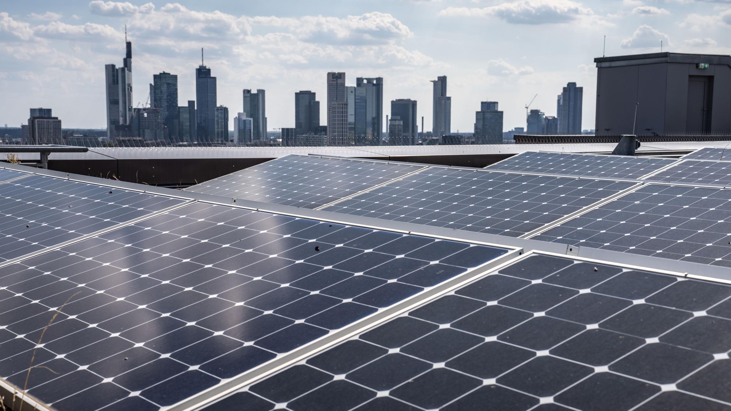 Solarmodule einer Photovoltaikanlage stehen auf dem Dach der Frankfurt School mit der Skyline der Stadt im Hintergrund.