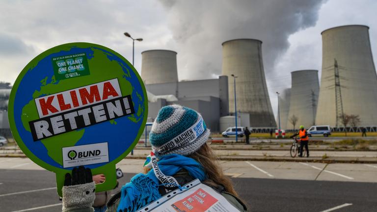 Vor dem Braunkohlekraftwerk Jaenschwalde hält 2019 eine Klimaaktivistin ein Schild mit der Aufschrift "KLIMA RETTEN!".