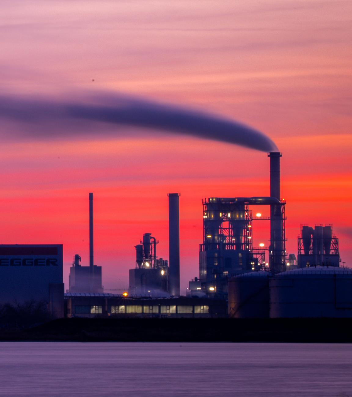  Dampf steigt aus den Schornsteinen der Holzwerke am Seehafen während die aufgehende Sonnen den Himmel orangerot einfärbt. 