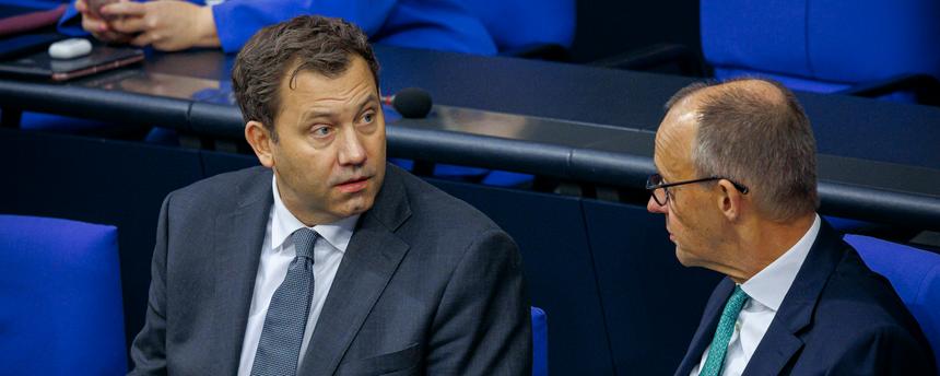 SPD-Chef Lars Klingbeil und Bundeskanzler Friedrich Merz (CDU) sitzen im Bundestag nebeneinander und sprechen miteinander.