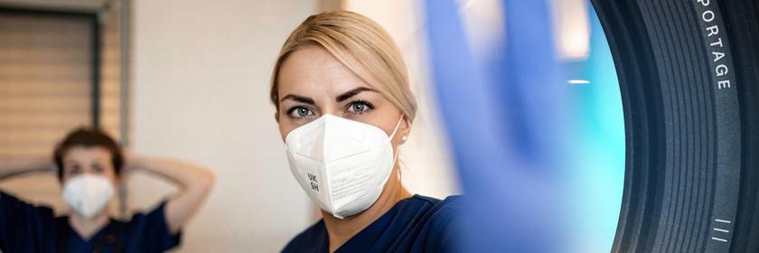 Krankenschwester hebt eine Hand zum Stopp, eine andere ist unscharf im Hintergrund zu sehen.
