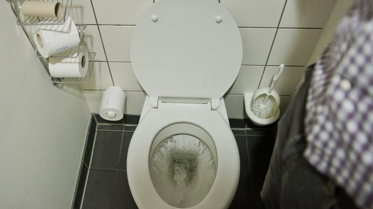 Ein Mann betätigt eine Toilettenspülung.