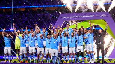 Das Team von Manchester City jubelt auf einer Bühne.