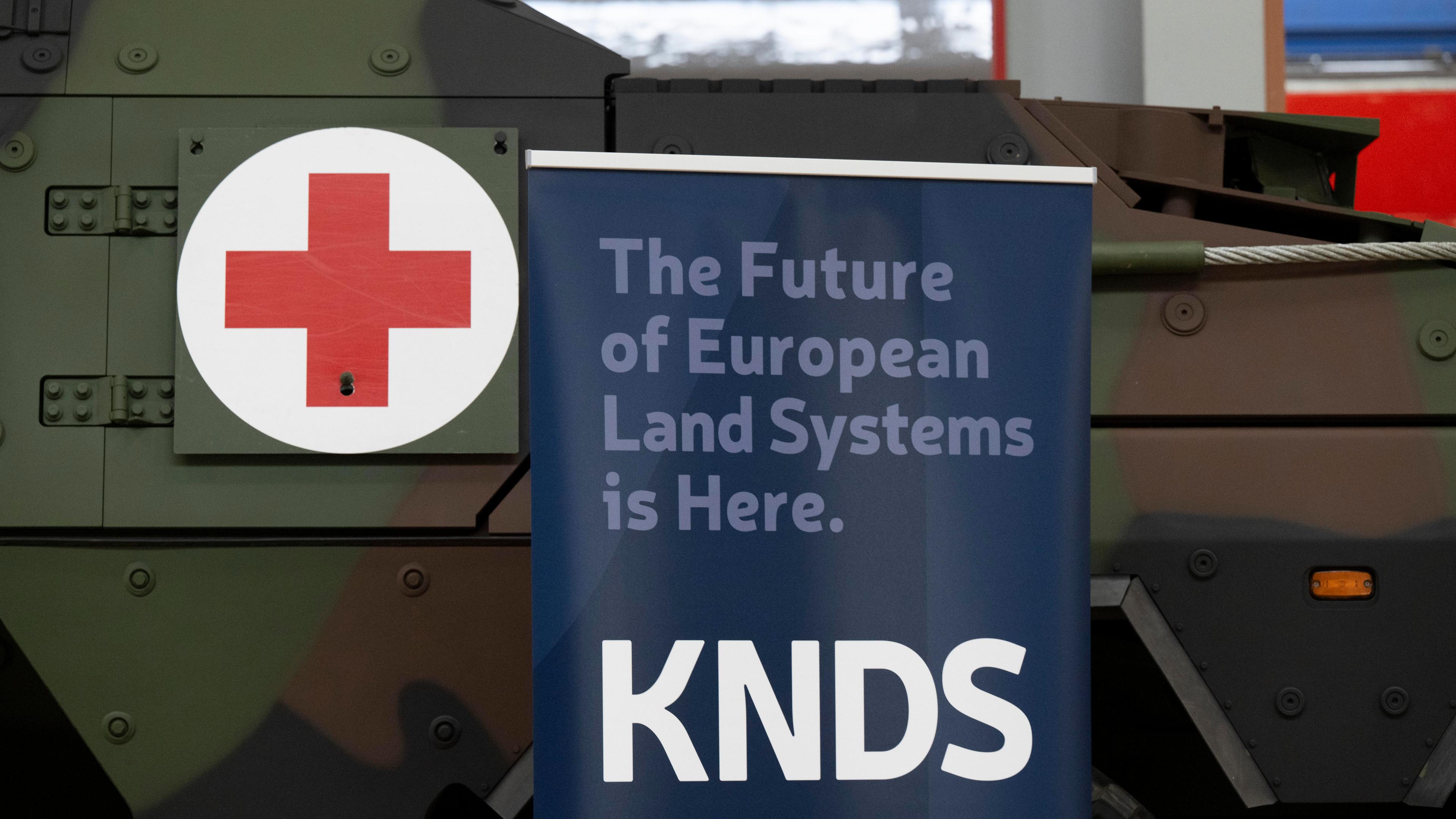 05.02.2025, Sachsen, Görlitz: Ein Banner mit dem Logo des deutsch-französischen Rüstungskonzerns KNDS steht während einer Informationsveranstaltung der Alstom Transportation Germany GmbH in einer Werkhalle vor einem gepanzerten Transport-Kraftfahrzeug.