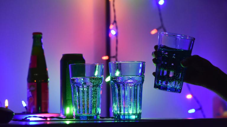 Gläser stehen auf einem Tresen, von denen eins in eine Hand genommen wird.