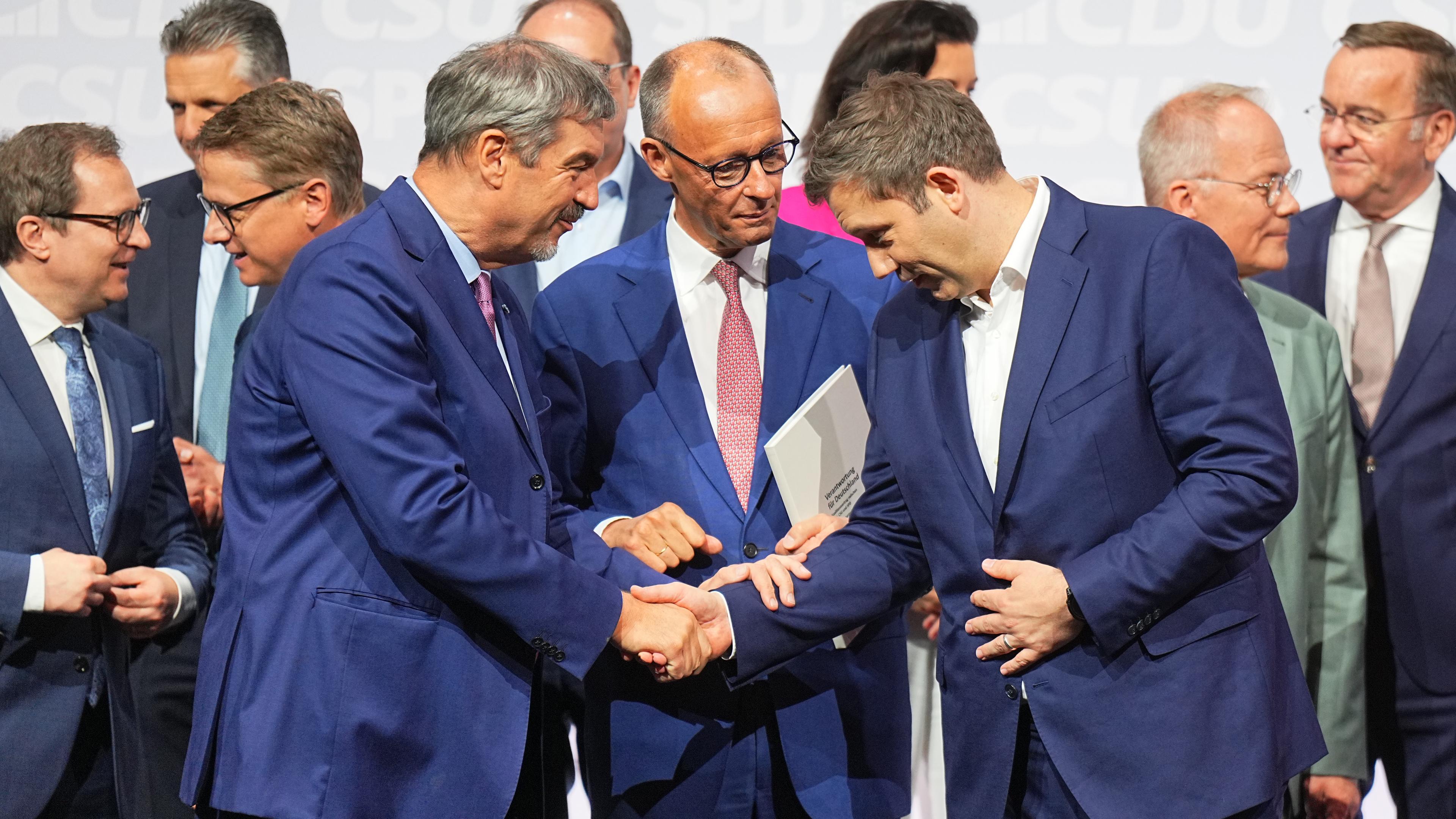 CDU-Vorsitzender und -Kanzlerkandidat Friedrich Merz (M), CSU-Vorsitzender Markus Söder (l) und SPD-Vorsitzender Lars Klingbeil, designierter Bundesfinanzminister und Vizekanzler, geben sich nach der Unterzeichnung des Koalitionsvertrags von CDU, CSU und SPD zhur Bildung einer neuen Bundesregierung im Euref-Campus die Hand.