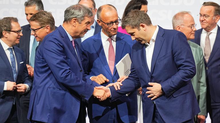 CDU-Vorsitzender und -Kanzlerkandidat Friedrich Merz (M), CSU-Vorsitzender Markus Söder (l) und SPD-Vorsitzender Lars Klingbeil, designierter Bundesfinanzminister und Vizekanzler, geben sich nach der Unterzeichnung des Koalitionsvertrags von CDU, CSU und SPD zhur Bildung einer neuen Bundesregierung im Euref-Campus die Hand.