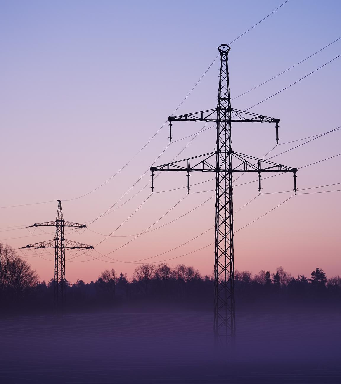 Nebel zieht über ein Solarfeld mit darüber laufender Stromleitungen.