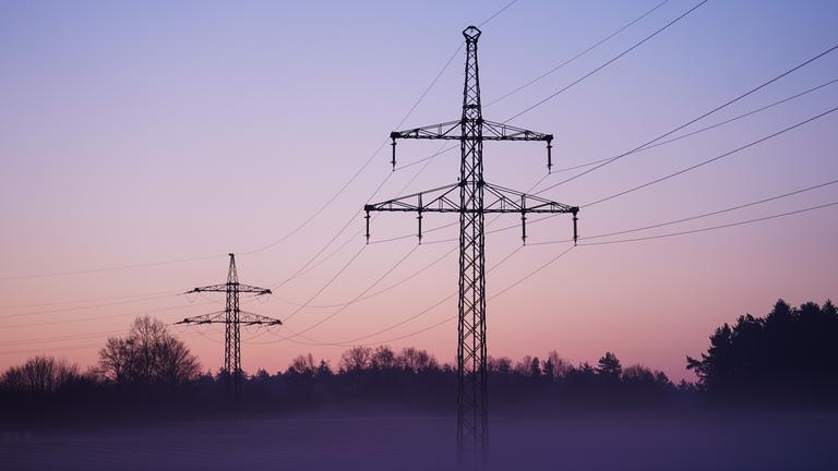 Nebel zieht über ein Solarfeld mit darüber laufender Stromleitungen.