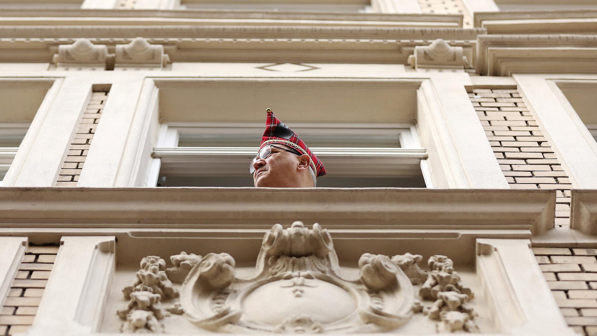 Ein Karnevalist mit Karnevalshut schaut aus einem Fenster der Aufstellung der Rosenmontagszüge zu.