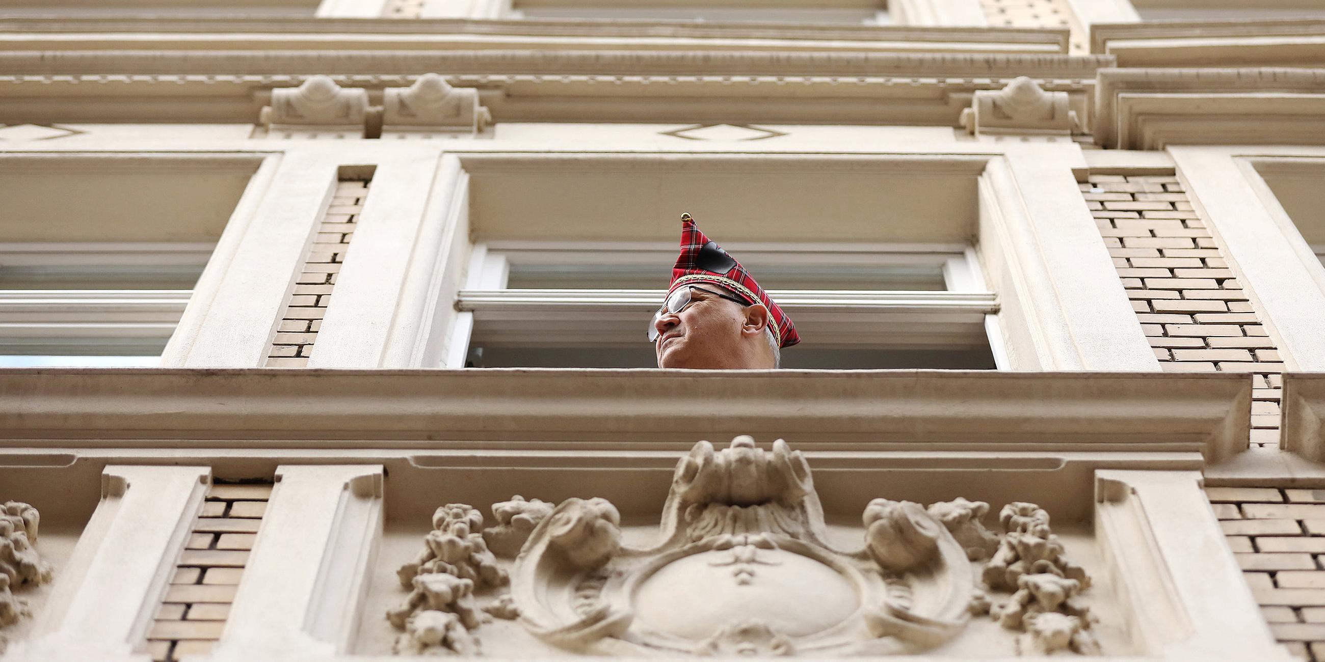 Ein Karnevalist mit Karnevalshut schaut aus einem Fenster der Aufstellung der Rosenmontagszüge zu.