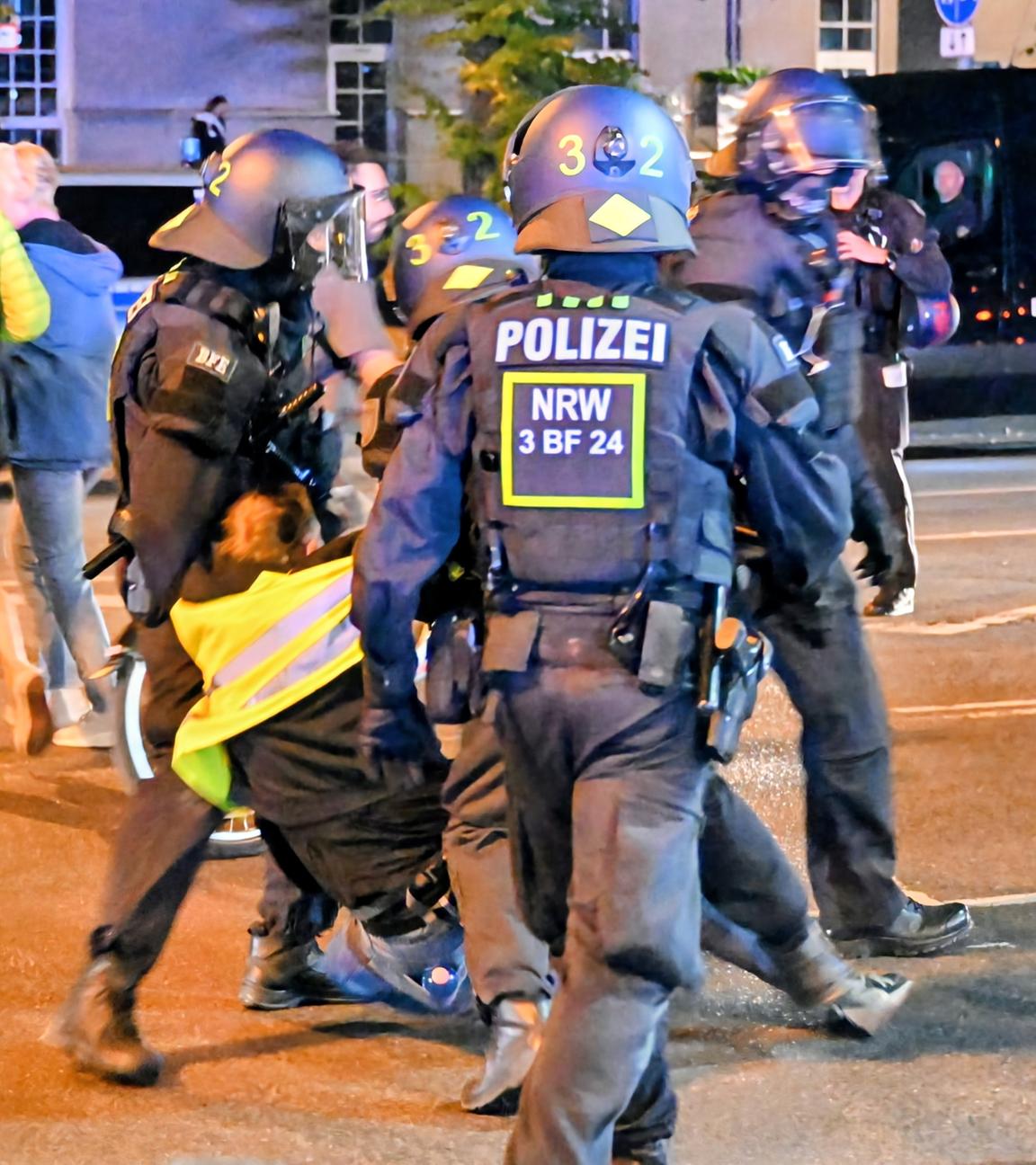 Mehrere Polizisten führen einen Demonstranten der Antikriegs-Demo in Köln ab. Er wehrt sich dagegen.