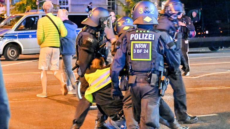 Mehrere Polizisten führen einen Demonstranten der Antikriegs-Demo in Köln ab. Er wehrt sich dagegen.