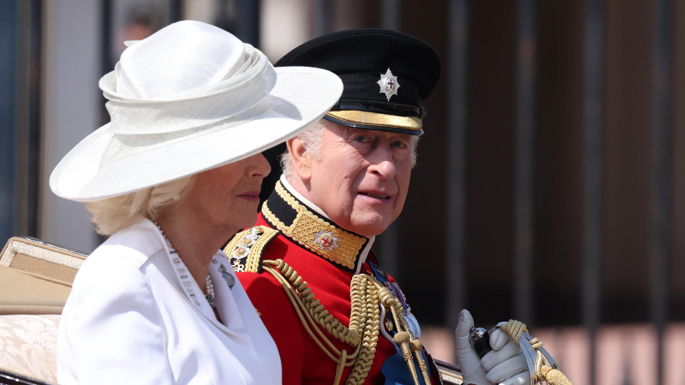 Königin Camilla und König Charles sitzen nebeneinader in einer offenen Kutsche