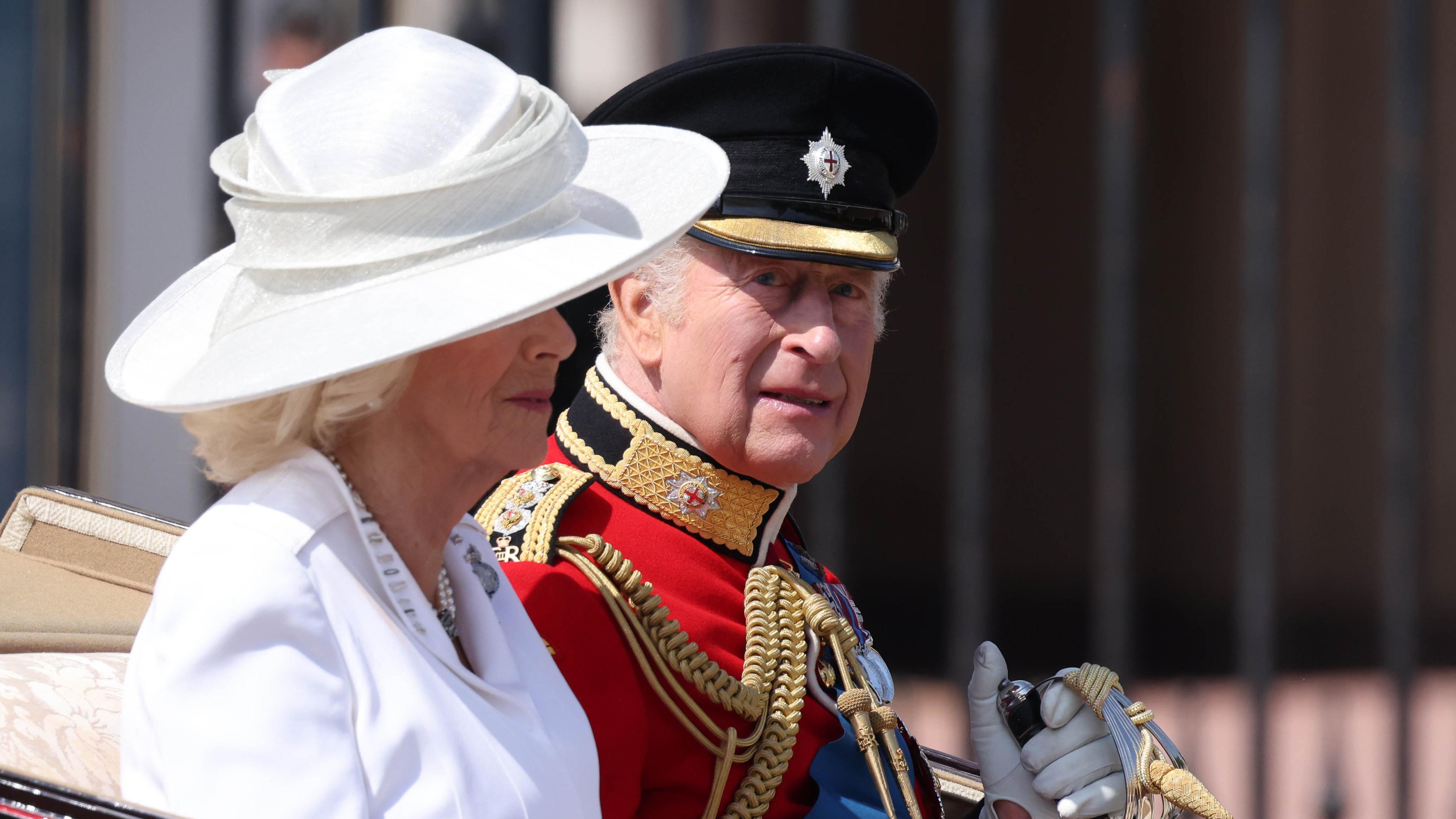 Königin Camilla und König Charles sitzen nebeneinader in einer offenen Kutsche