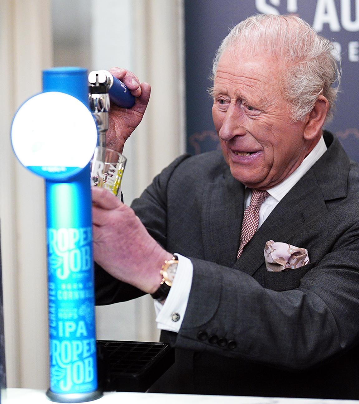 König Charles (links) zapft ein Bier, seine Frau Camilla steht neben ihm und freut sich darüber. 