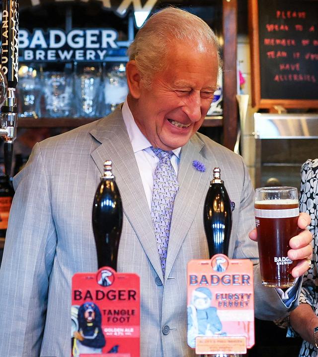 König Charles (rechts) zapft ein Bier, neben ihm steht seine Frau Königin Camilla.