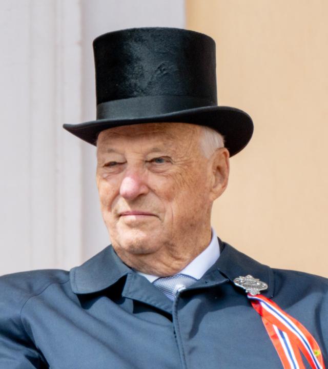 Auf dem Bild ist König Harald zu sehen. Er trägt einen schwarzen Zylinder und einen dunkelblauen Mantel mit einer rot-weiß-blauen Schleife.