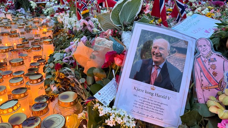 Eine Trauerkarte mit einem Bild von König Harald in Mitten von Kerzen und Blumen. 