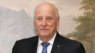 Das Bild zeigt König Harald V. von Norwegen vor einem Gemälde mit einem Berg und einem Baum.