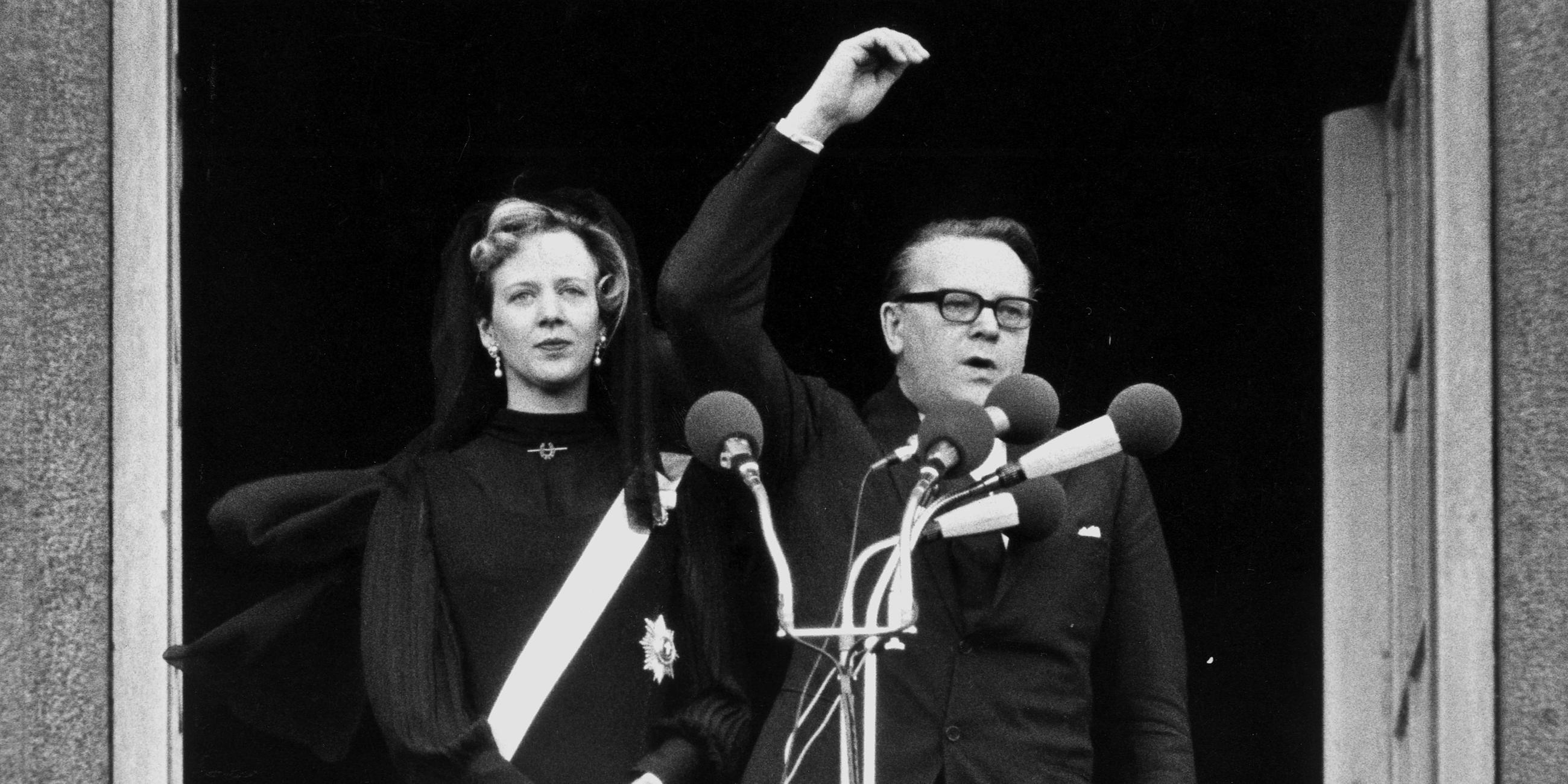 Ein schwarz-weiß Bild aus dem Jahre 1972. Zu sehen ist Margrethe II. von Dänemark, die neben dem Premierminister Jens Otto Krag auf einem Balkon steht und zur Königin ernannt wird.