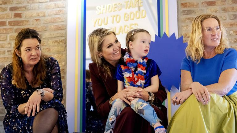 Königin Maxima bei einer Kindermodenshow mit einem Kind auf dem Schoß, das zuvor vom Laufsteg gefallen war.
