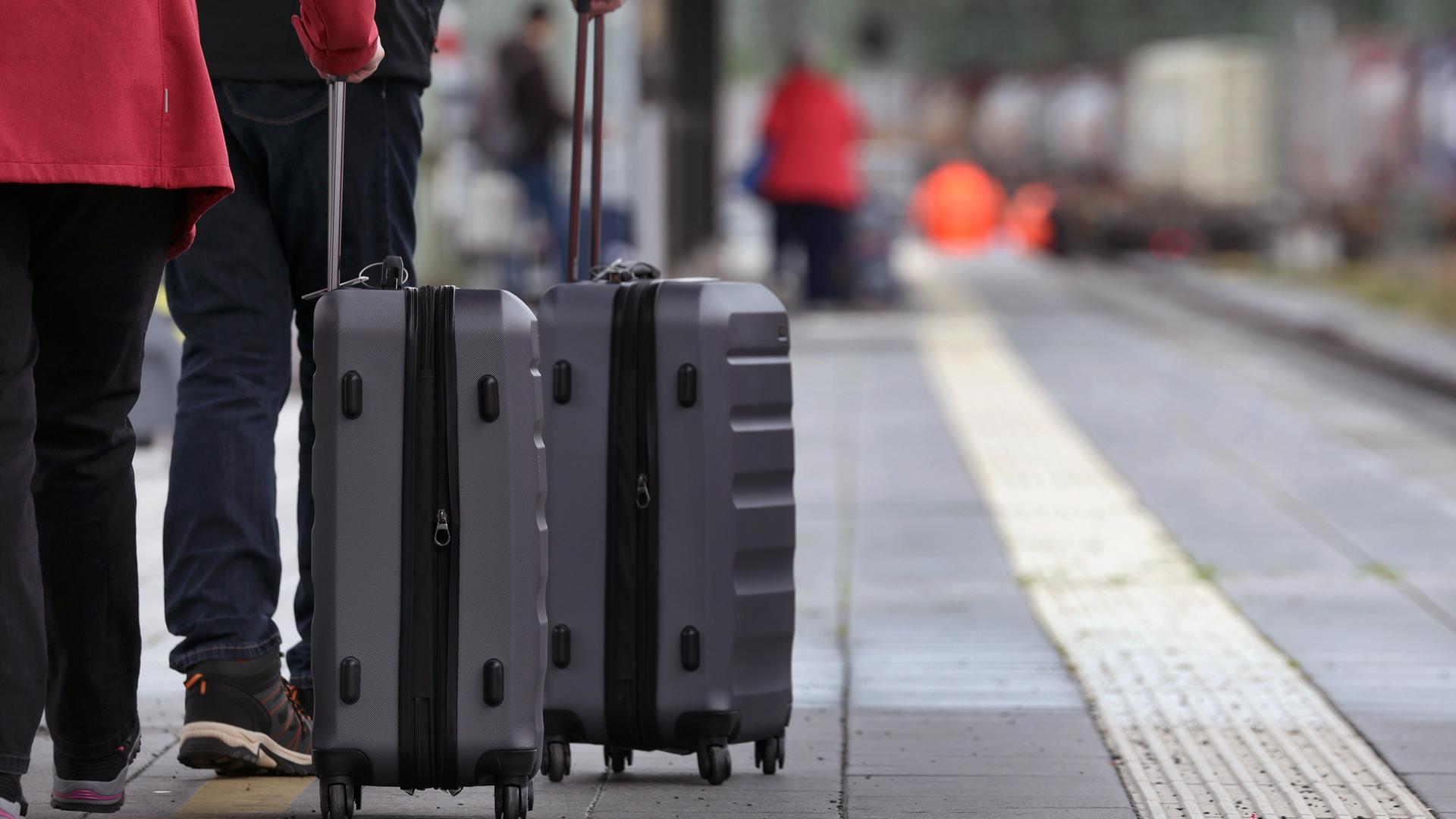 Reisende mit Koffern warten im Hauptbahnhof auf einem Bahnsteig.