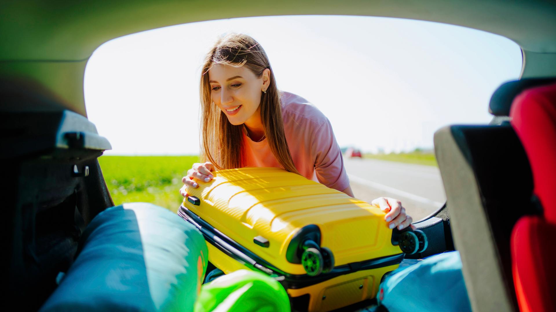 Frau verstaut Gepäck im Kofferraum.