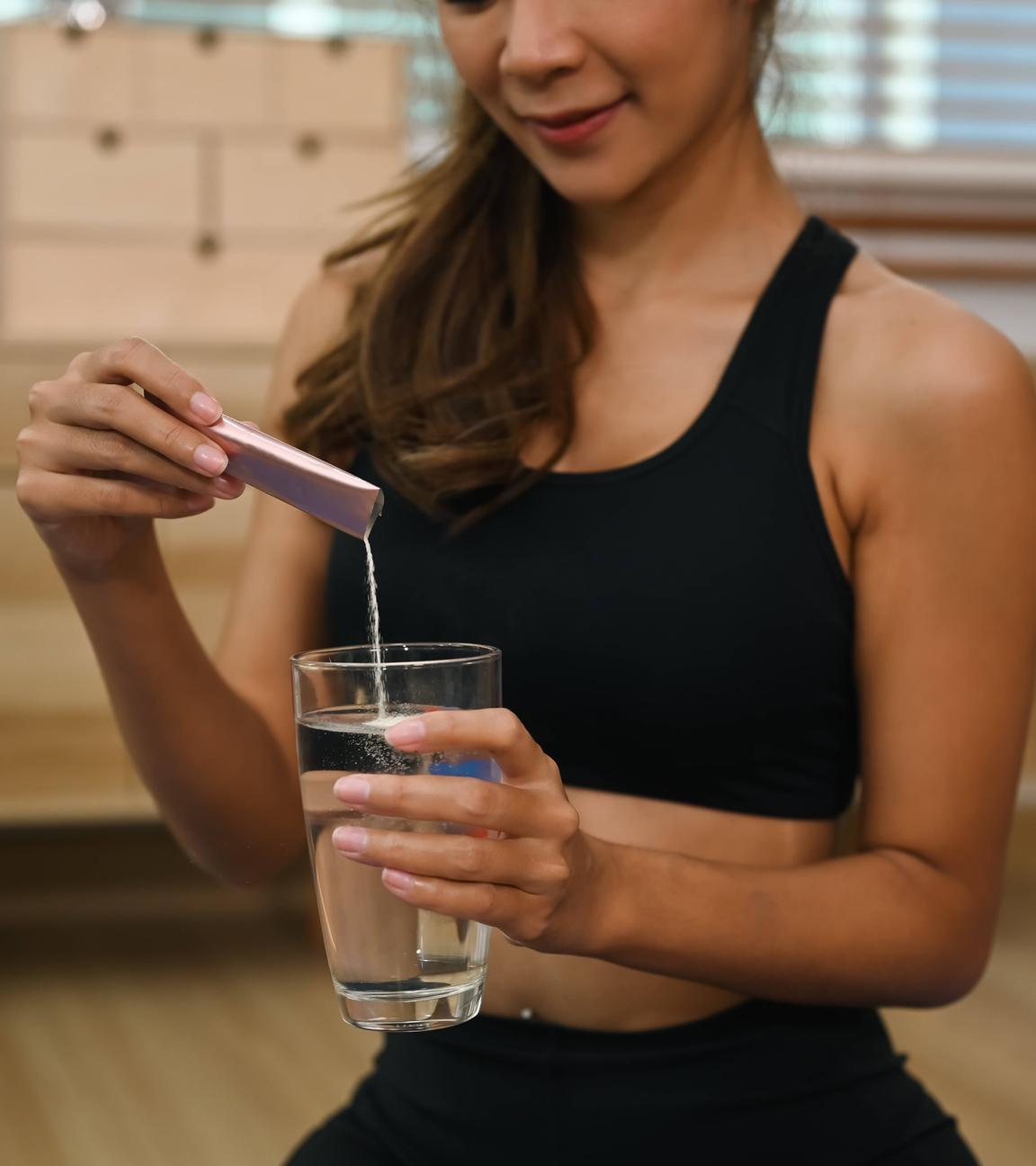 Eine Frau gibt Kollagenpulber aus einem Tütchen in ein Glas Wasser.
