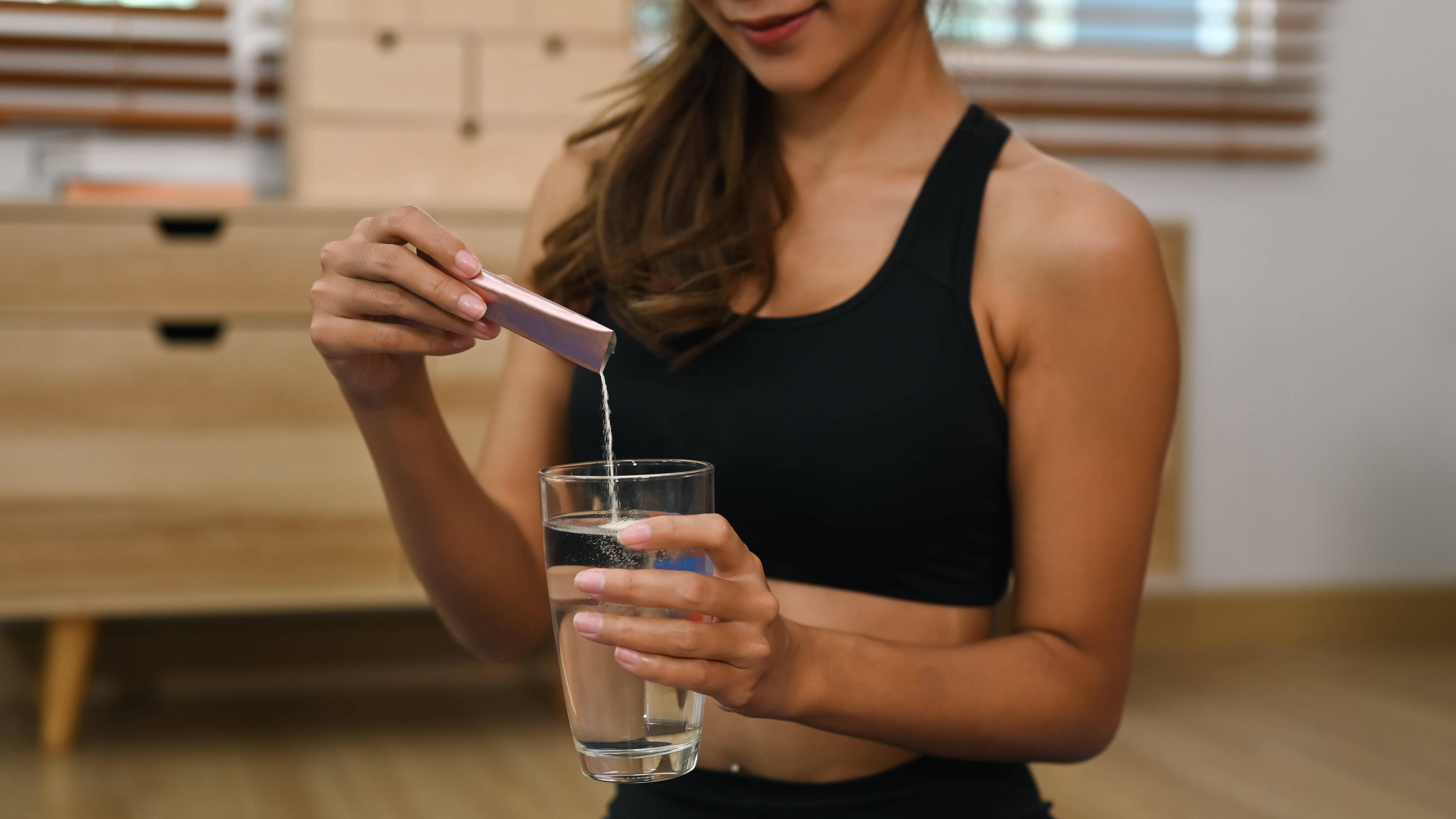 Eine Frau gibt Kollagenpulber aus einem Tütchen in ein Glas Wasser.