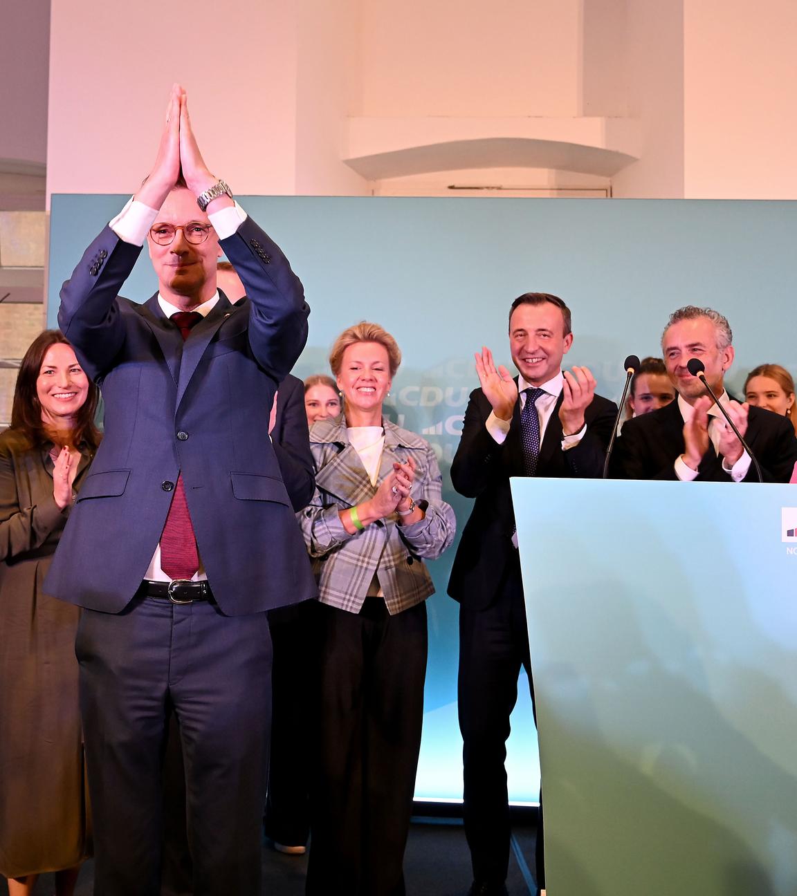 Ministerpräsident Hendrik Wüst ( CDU ) hebt die Arme nach seinem Statement. Im Hintergund ist das Logo und weitere Vertreter der CDU.