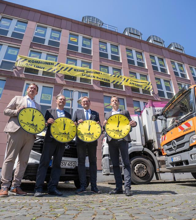 Thomas Przybylla, stellvertretender Vorsitzender des Gemeinde- und Städtebundes Rheinland-Pfalz, Daniel Köbler, Bürgermeister von Mainz, Markus Zwick, Vorsitzender des Städtetages Rheinland-Pfalz, und Nino Haase, Oberbürgermeister von Mainz, stehen zusammen und weisen mit symbolischen Uhren auf die Finanzlage der Kommunen hin.