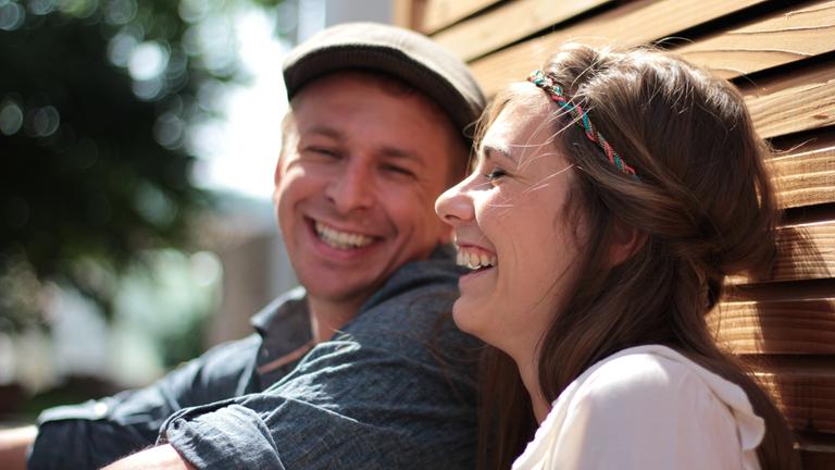 Ein Mann und eine Frau sitzen nebeneinander und lachen.