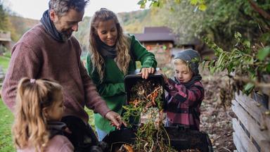 Eine Familie wirft Küchenabfälle auf einen Komposthaufen im Garten.