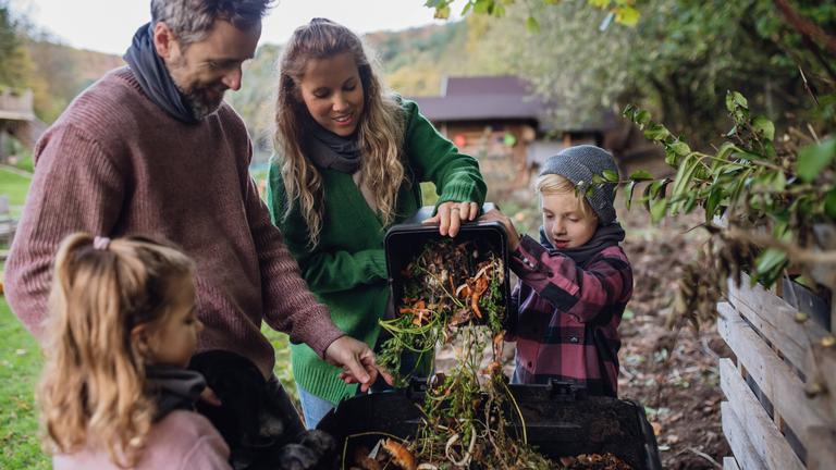 Eine Familie wirft Küchenabfälle auf einen Komposthaufen im Garten.