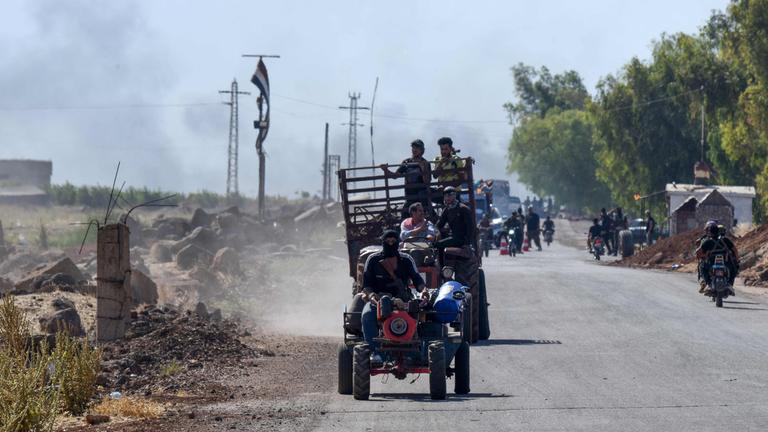 Rauch steigt von gemeldeten Kämpfen auf, als Kämpfer von Beduinenstämmen am 18. Juli 2025 auf einer Straße im Dorf al-Mazraa in die überwiegend von Drusen bewohnte Stadt Suweida im Süden Syriens fahren. 
