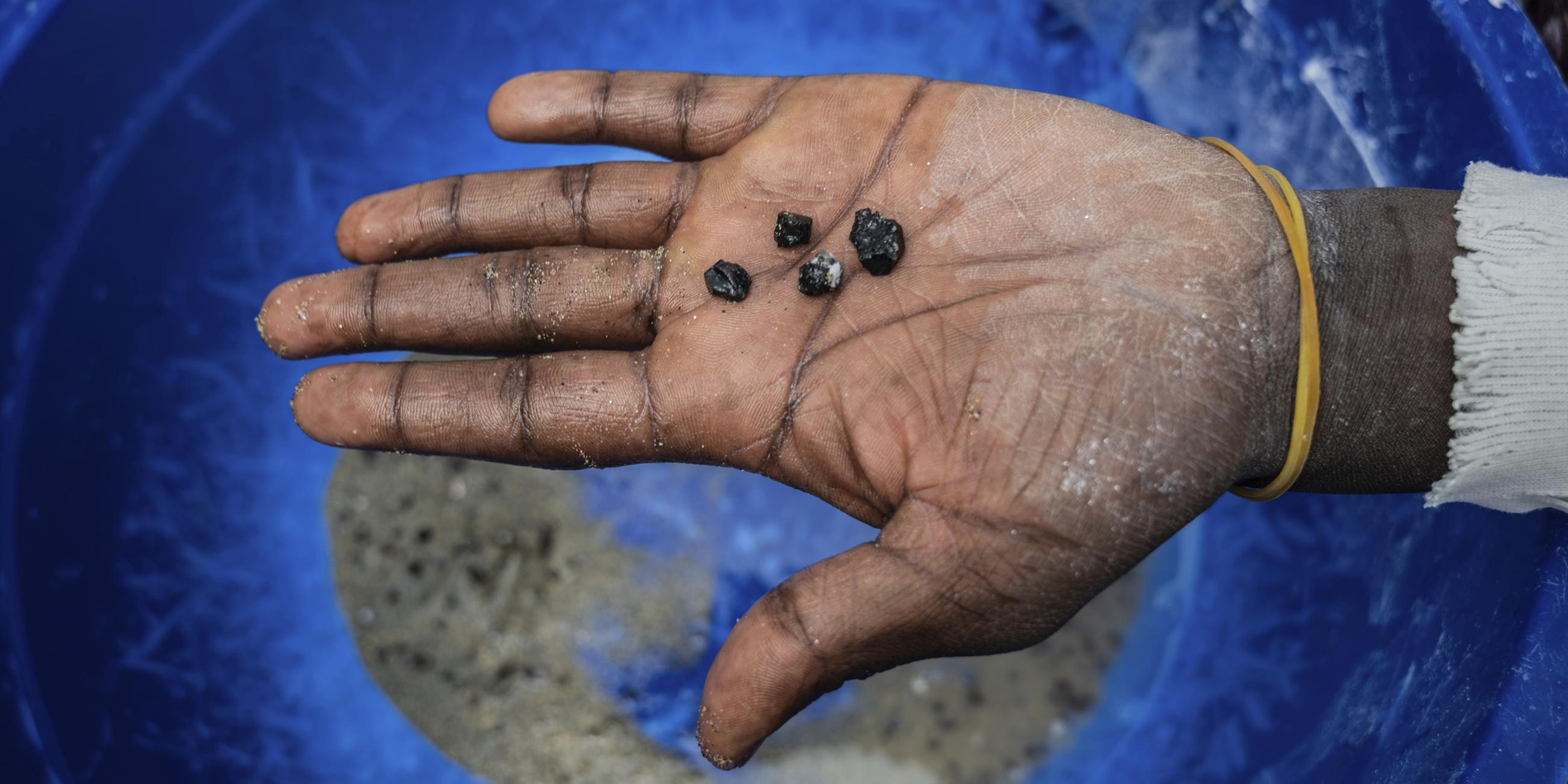 Ein Bergarbeiter hält Stücke von Coltan-Erz in der Hand