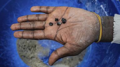 Ein Bergarbeiter hält Stücke von Coltan-Erz in der Hand