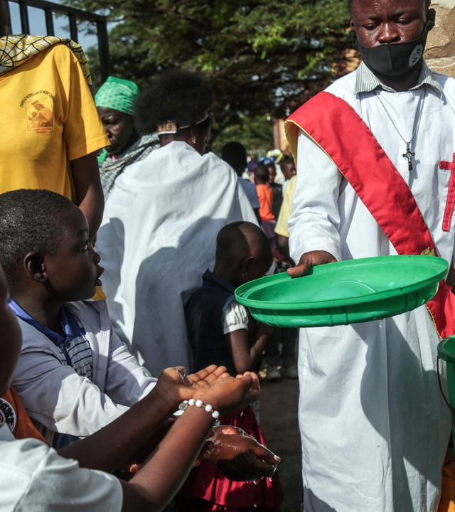 Ein Diakon hilft jungen Gemeindemitgliedern beim Händewaschen vor dem Betreten der Kirche in Bunia, 24. Mai 2026.