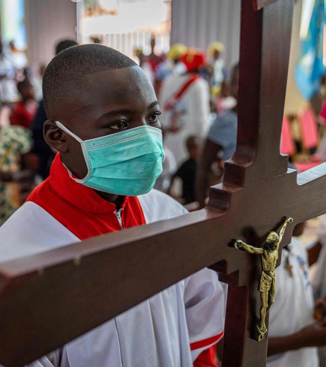 Ein Ministrant trägt während eines Gottesdienstes in der Kathedrale von Bunia am 24. Mai 2026 ein Kreuz und eine Maske.